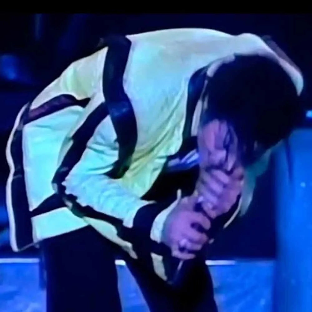 Person in a light-colored outfit with suspenders holding a microphone on a stage with blue lighting.