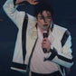 Person in a white and black jacket holding a microphone against a dark background