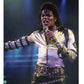 Person in a white jacket with black arm bands and a studded belt, holding a microphone on stage.
