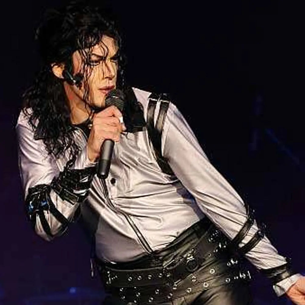 Person in a white shirt and black leather outfit holding a microphone on a dark background