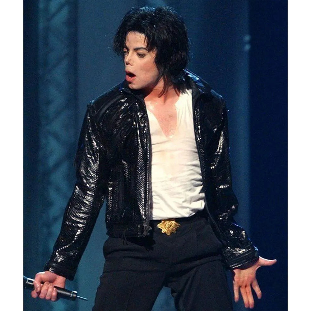 Person wearing a shiny black jacket on stage with a blue curtain background